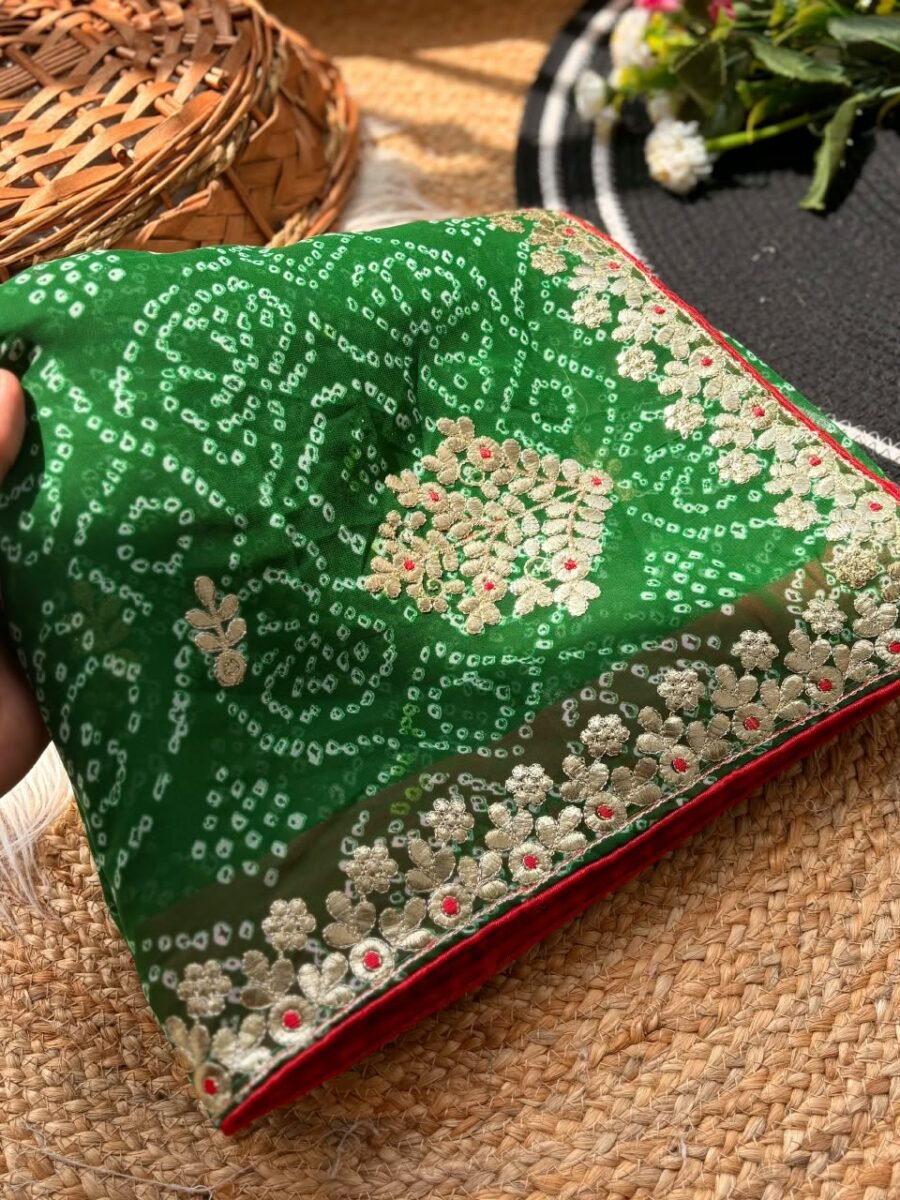 A person holds a green Bandhani Georgette saree with gold Gota Patti embroidery on a rustic background.