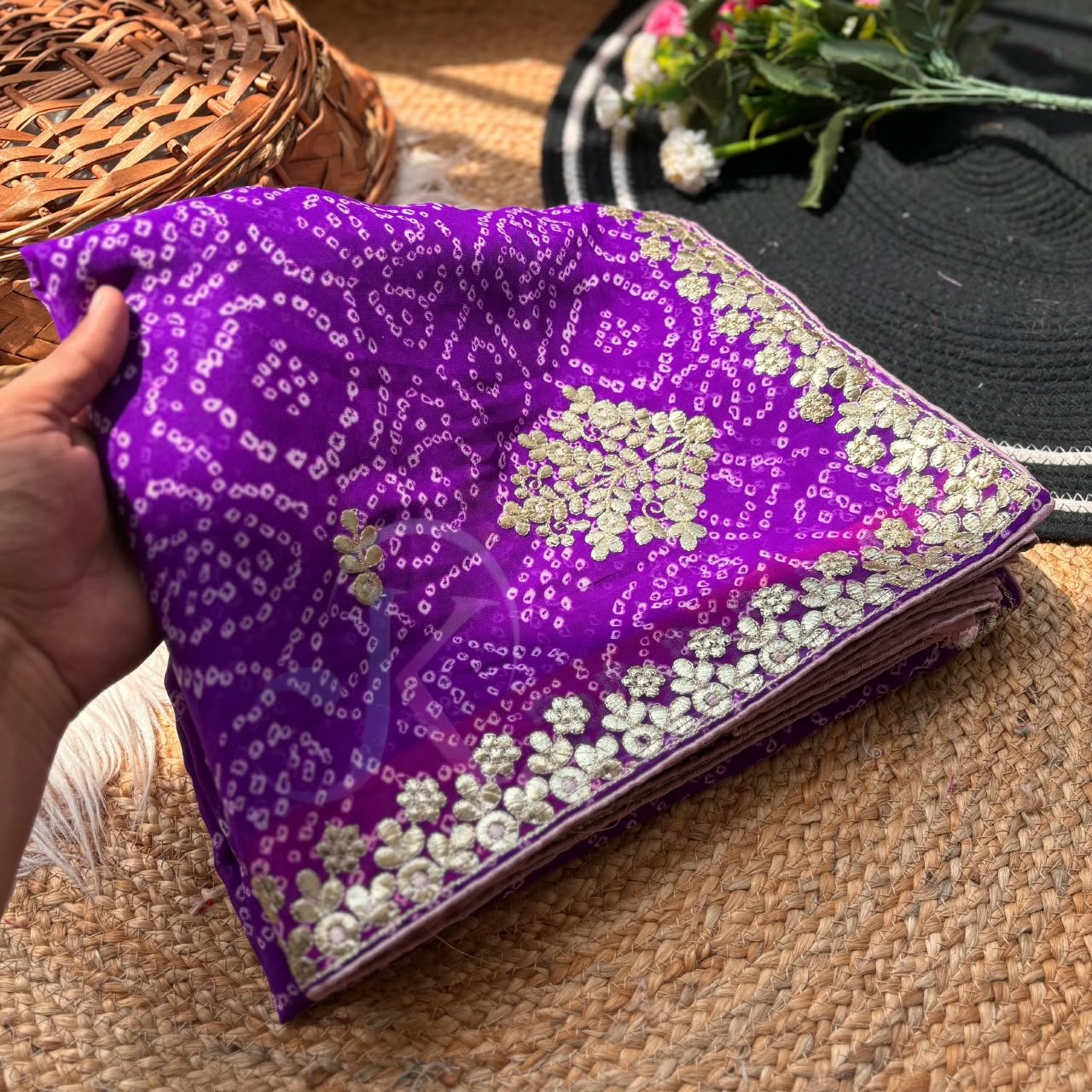 Deep Green Bandhani Georgette Saree With Gota Patti Work 4 A person holds a green Bandhani Georgette saree with gold Gota Patti embroidery on a rustic background.