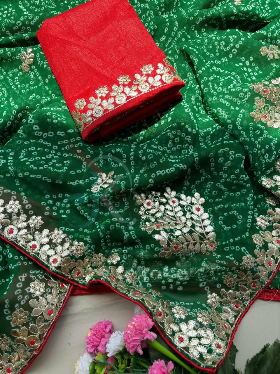 Deep Green Bandhani Georgette Saree With Gota Patti Work 5 A person holds a green Bandhani Georgette saree with gold Gota Patti embroidery on a rustic background.