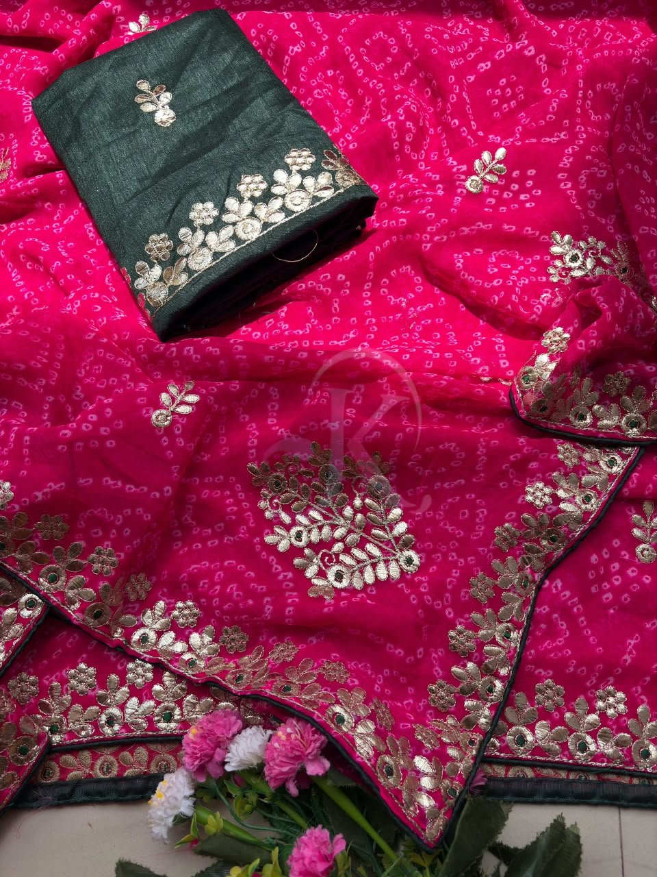 Deep Green Bandhani Georgette Saree With Gota Patti Work 6 A person holds a green Bandhani Georgette saree with gold Gota Patti embroidery on a rustic background.