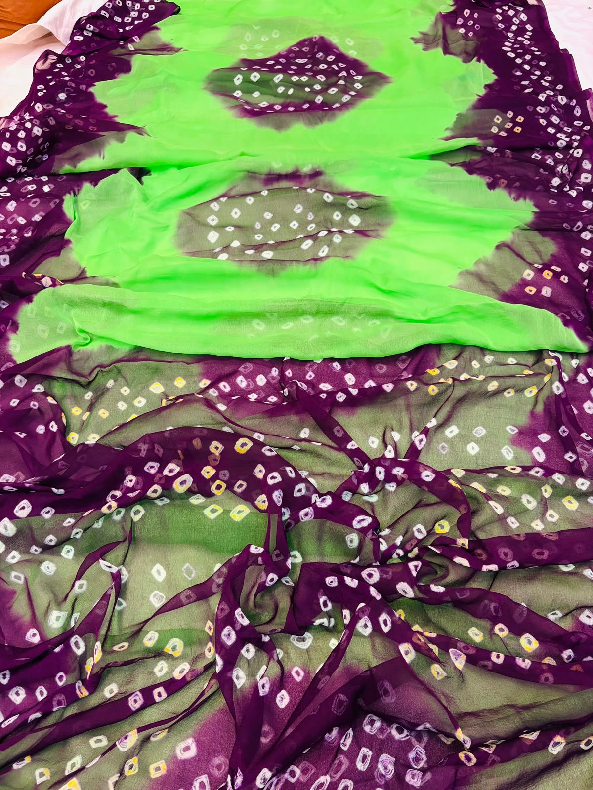 Nazneen Chiffon Hand Tie Dye Bandhani Saree 5 A close-up of a Nazneen Chiffon saree featuring a striking hand tie dye Bandhani pattern in yellow and maroon.