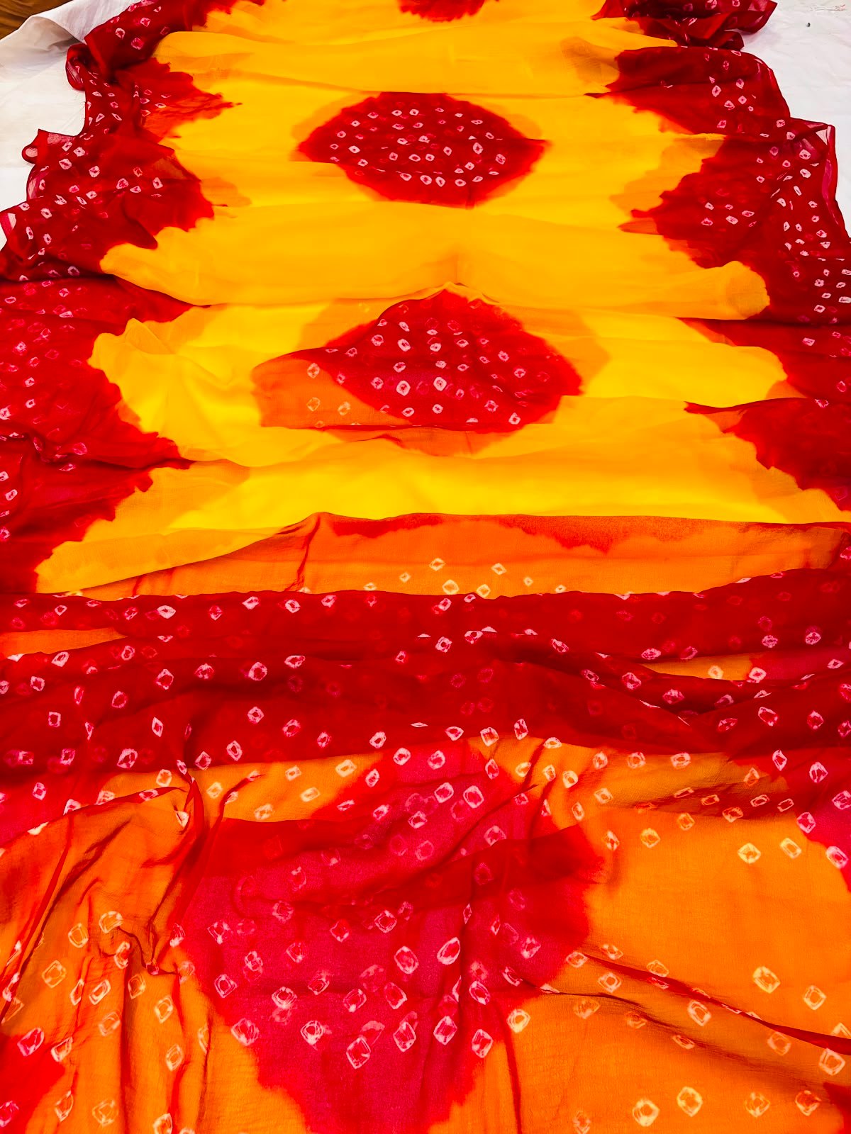 Nazneen Chiffon Hand Tie Dye Bandhani Saree 6 A close-up of a Nazneen Chiffon saree featuring a striking hand tie dye Bandhani pattern in yellow and maroon.