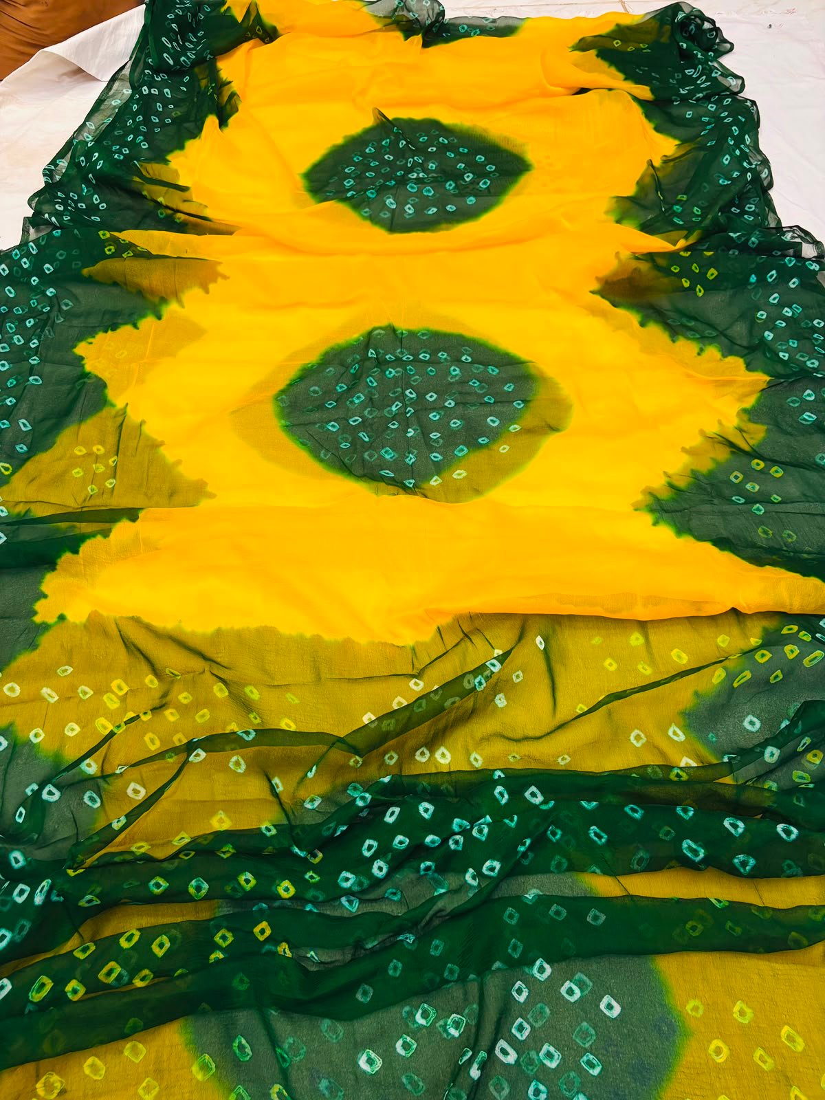 Nazneen Chiffon Hand Tie Dye Bandhani Saree 7 A close-up of a Nazneen Chiffon saree featuring a striking hand tie dye Bandhani pattern in yellow and maroon.
