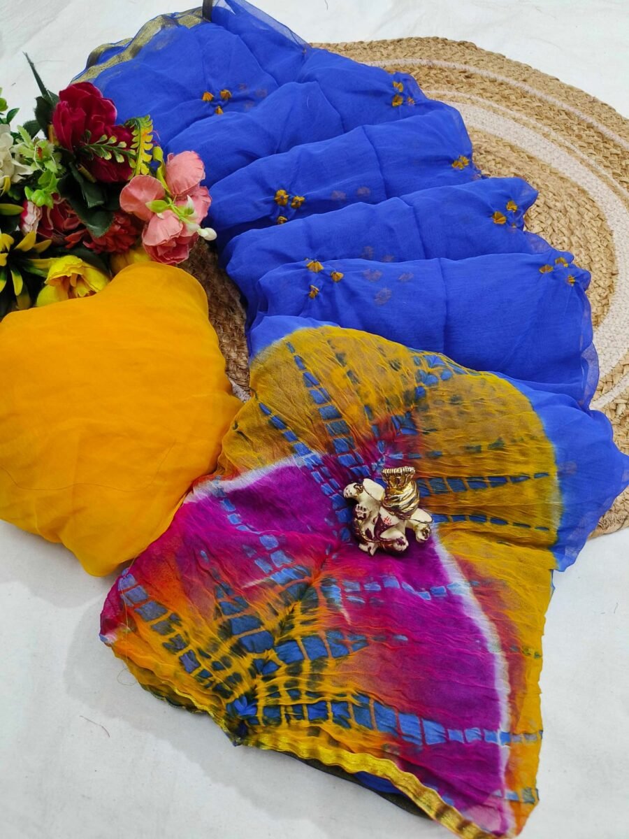A beautiful blue and multi-colored tie dye chiffon saree displayed with a yellow blouse piece and flowers on a textured mat.
