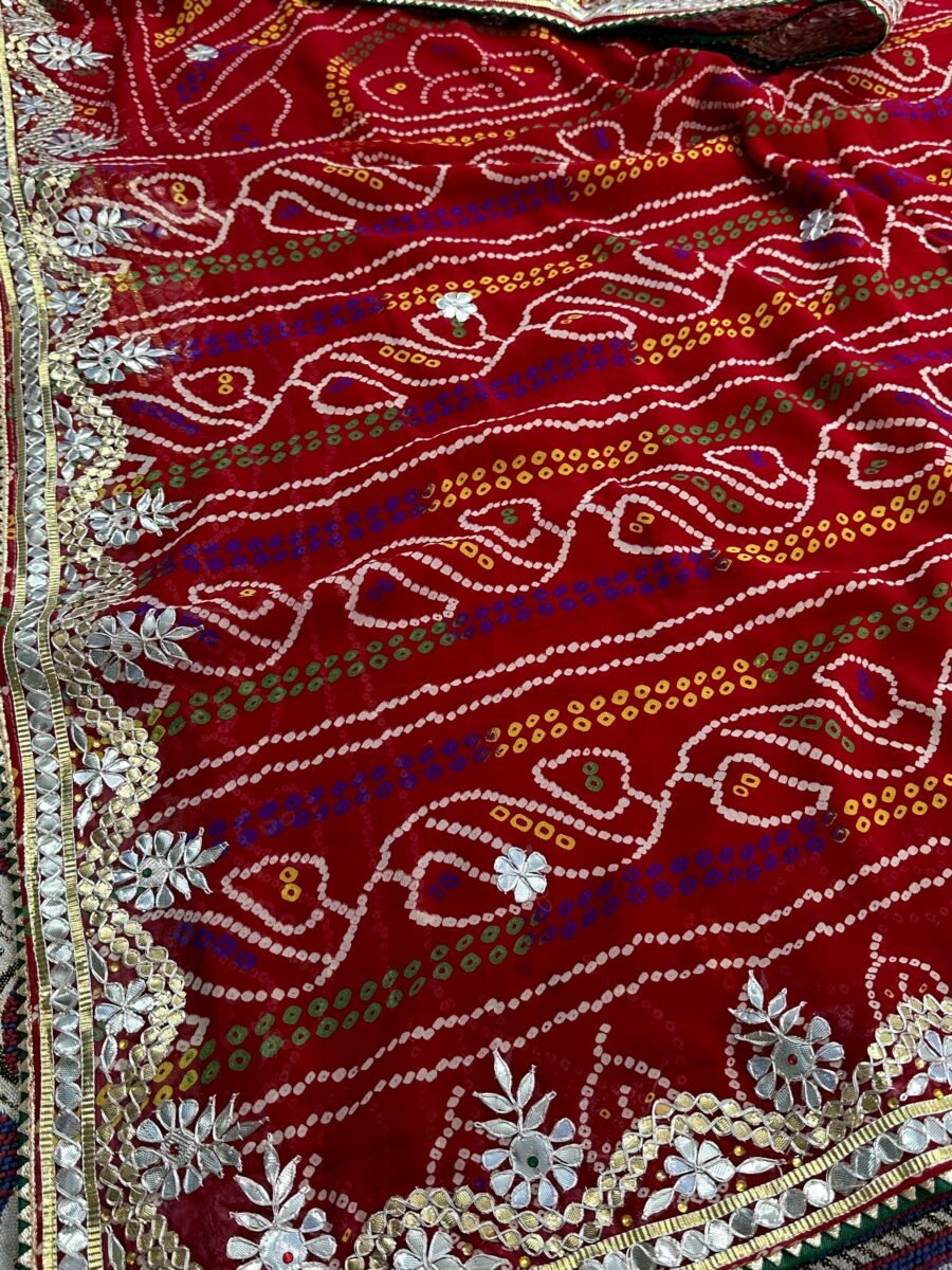 A close-up of a red Micro Georgette Chunari Saree featuring detailed Gota Patti border work and traditional bandhani-style patterns.