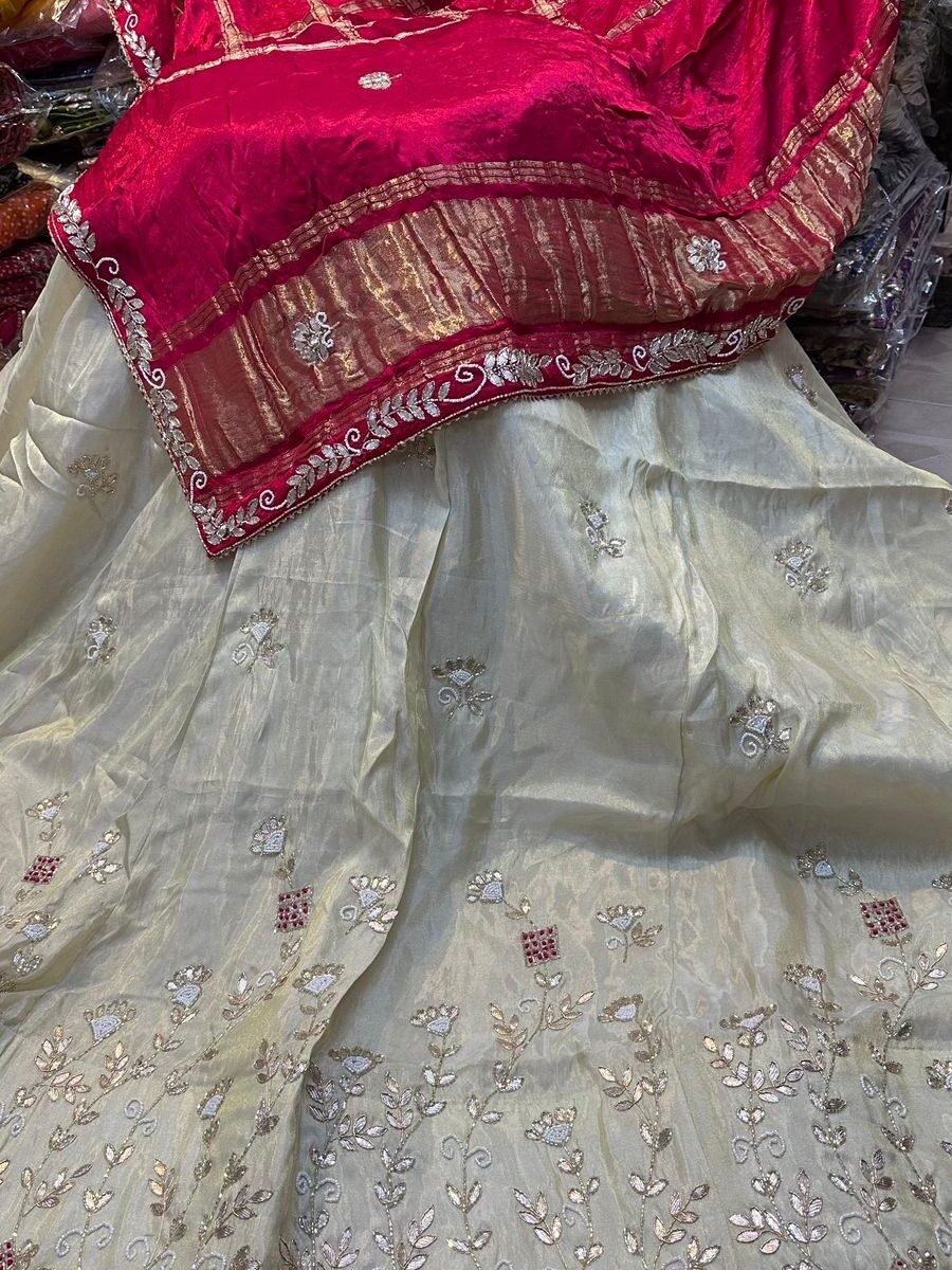 A beautiful cream-colored silk lehenga featuring intricate jardoji handwork paired with a vibrant red embroidered dupatta.