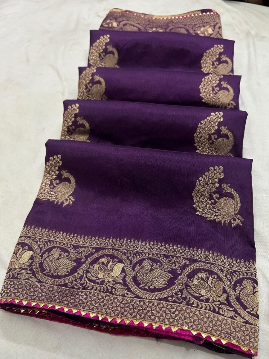 A beautiful deep purple Dola silk saree displayed in folds, showcasing gold zari peacock motifs and an ornate zari border.