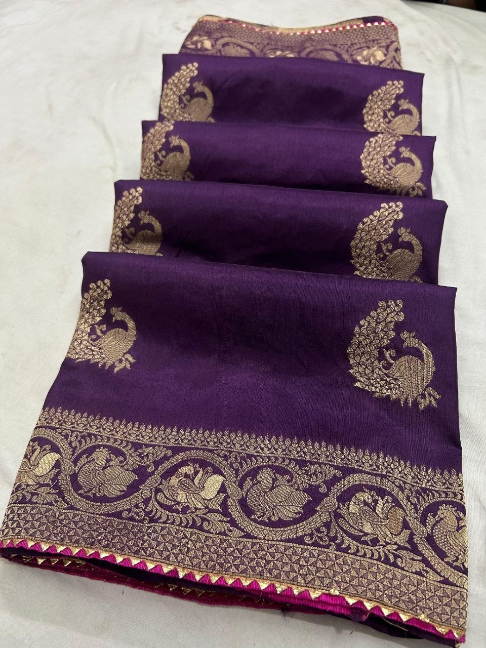 Deep Purple Dola Silk Saree with Peacock Zari Work 1 A beautiful deep purple Dola silk saree displayed in folds, showcasing gold zari peacock motifs and an ornate zari border.