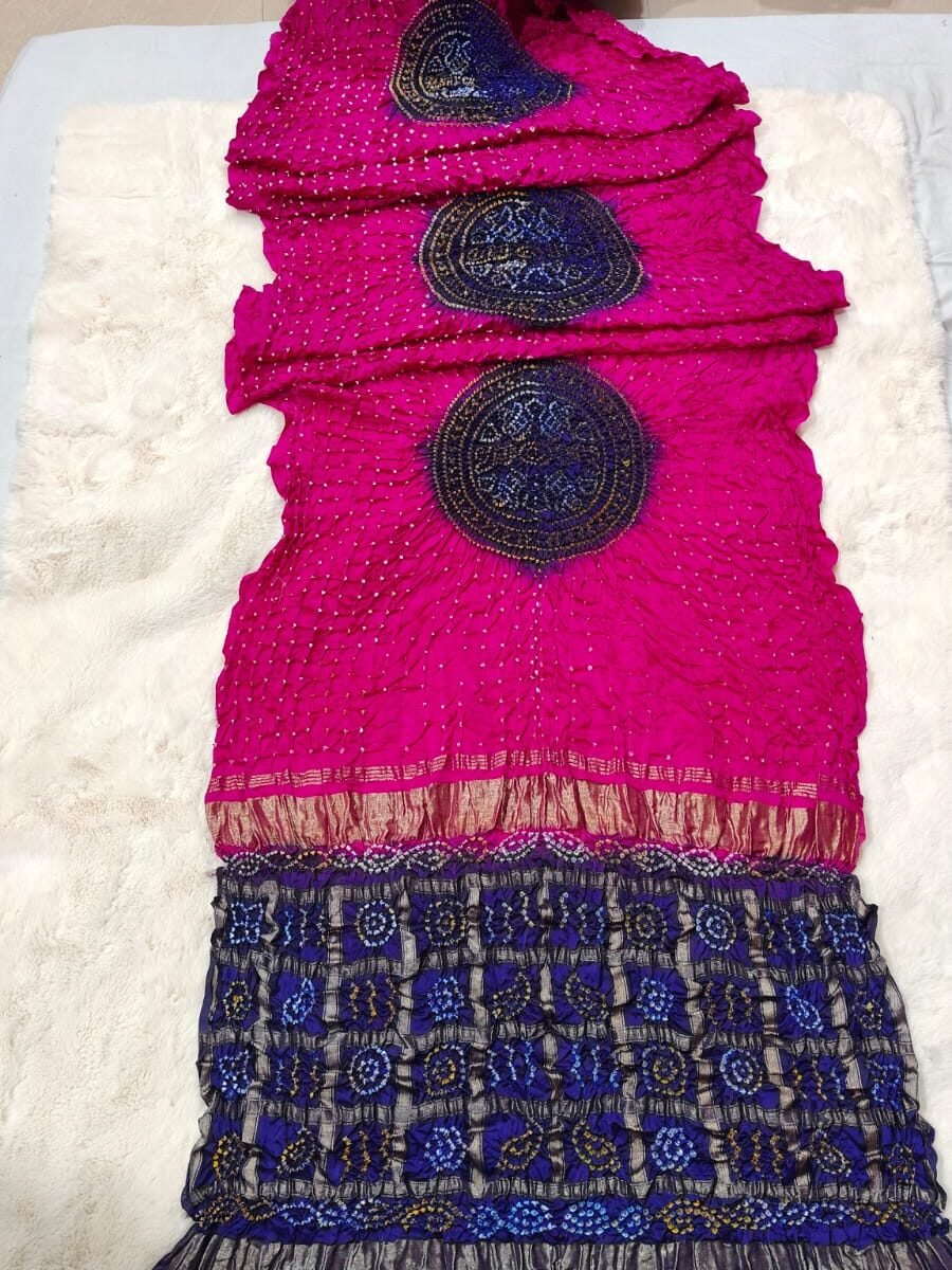 A beautiful bright pink Bandhej saree made from pure gajji moddal silk with a deep blue zari pallu displayed on a soft white background.