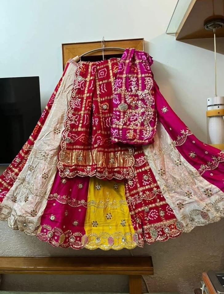 A beautiful silk Gharchola lehenga choli with intricate Gota Patti handwork displayed on a hanger.