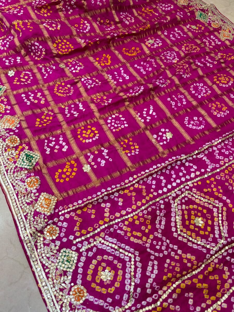 A close-up of a magenta Modal Gajji Silk Ghat Choola Bandhej saree featuring intricate hand Gota Patti work and a checkered pattern.