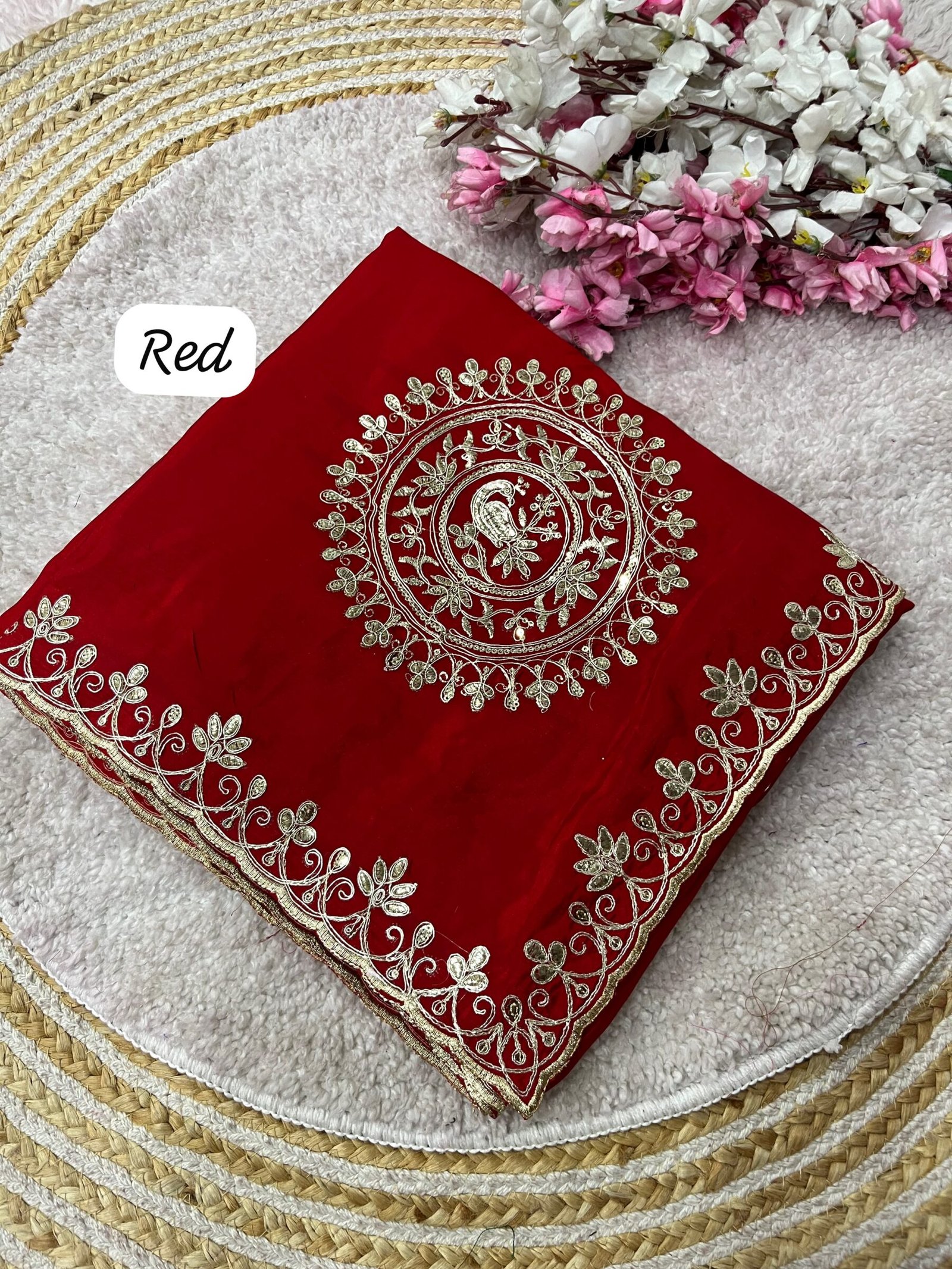 H.O Silk Gota Patti Saree 5 Four folded H.O silk sarees in blue, purple, and red displayed on a round woven mat with white and pink flowers.