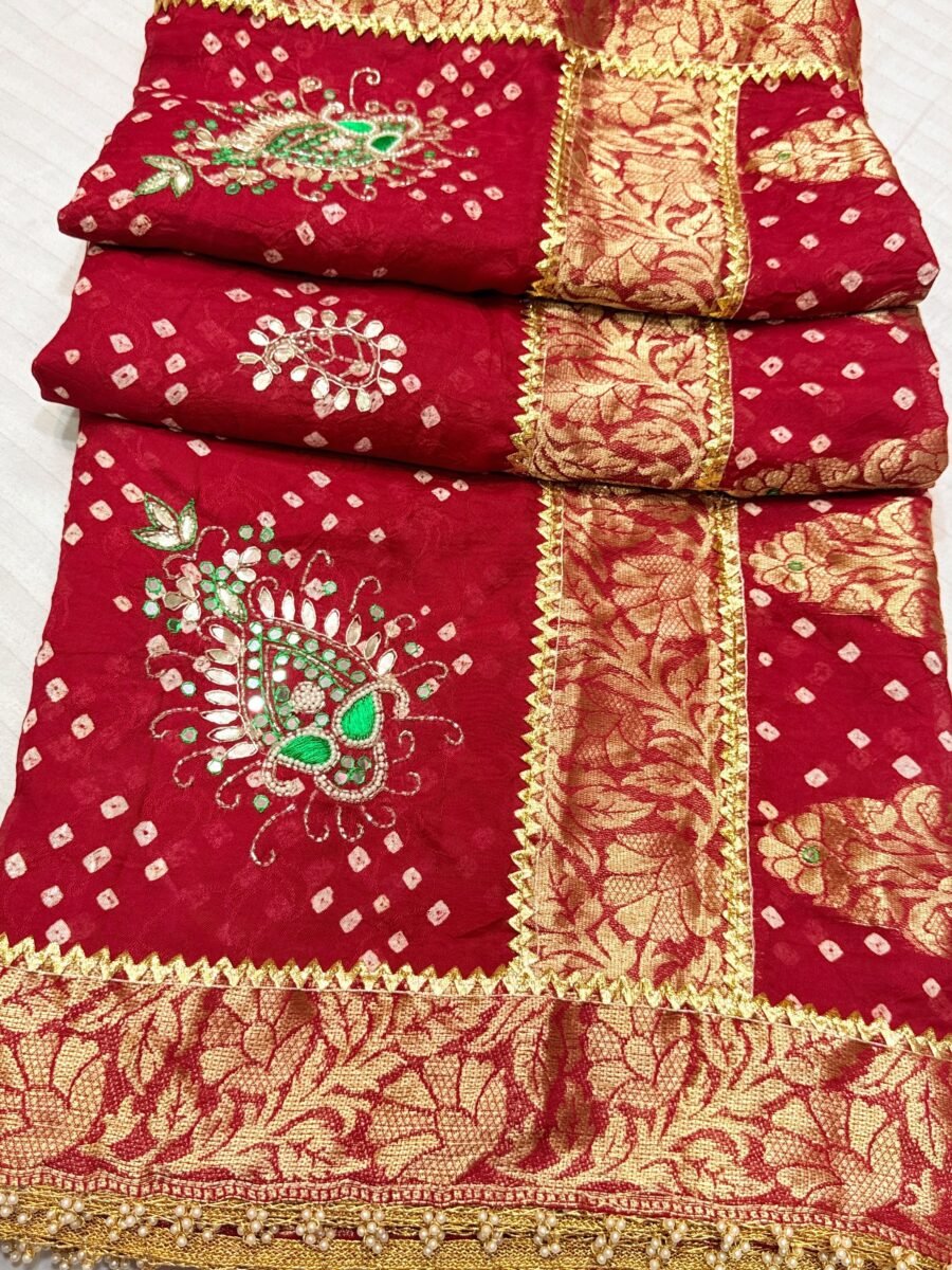 A close-up of a luxurious red Jamnagari Modal Gajji Silk saree featuring detailed hand-work, zari borders, and elegant moti latkans.