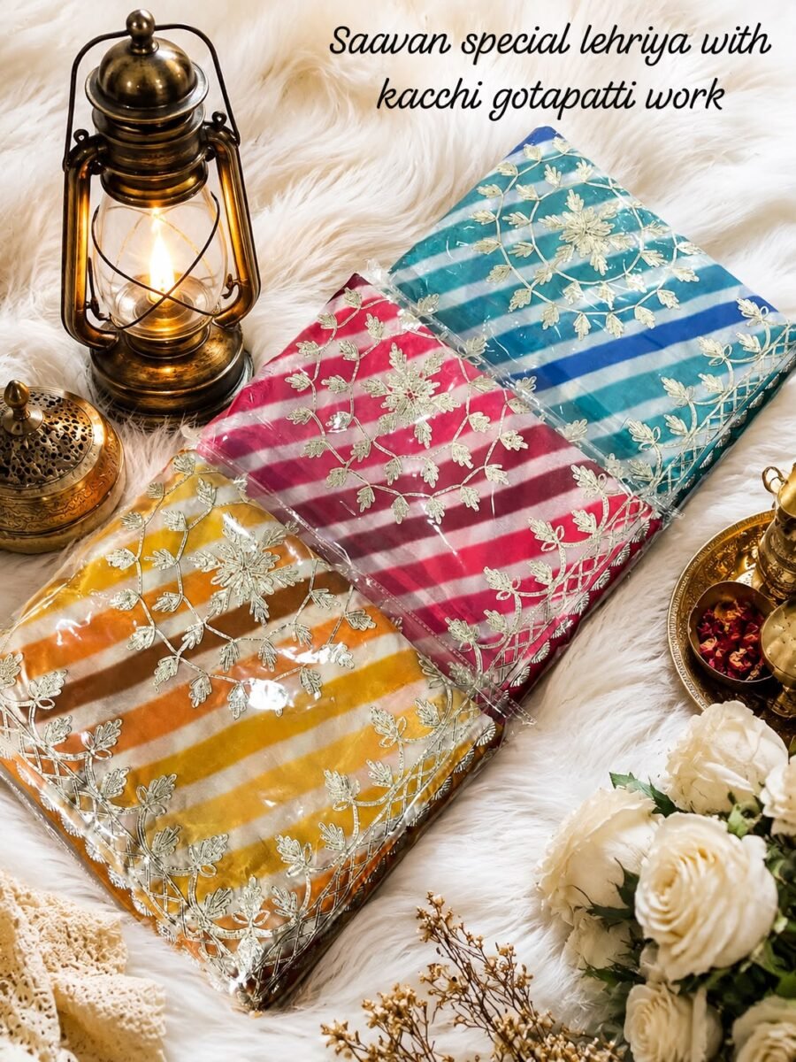 Three folded Leheriya sarees in vibrant colors with Kacchi Gotapatti work placed near a vintage lantern and white roses.