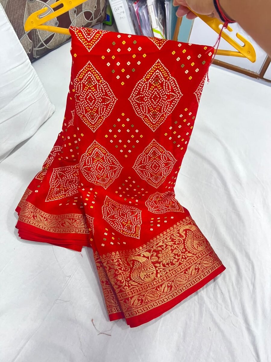 A vibrant red Marshmellow Bandhani saree with traditional patterns and a wide ornate gold woven border hanging on a yellow hanger.
