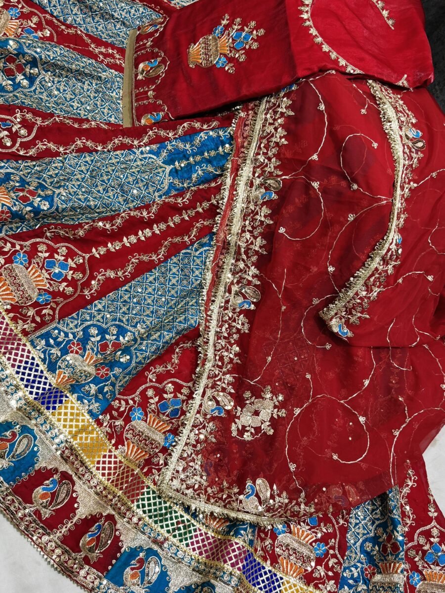A luxurious red Rajputi Poshak featuring intricate blue and gold traditional embroidery with a matching Odhani.