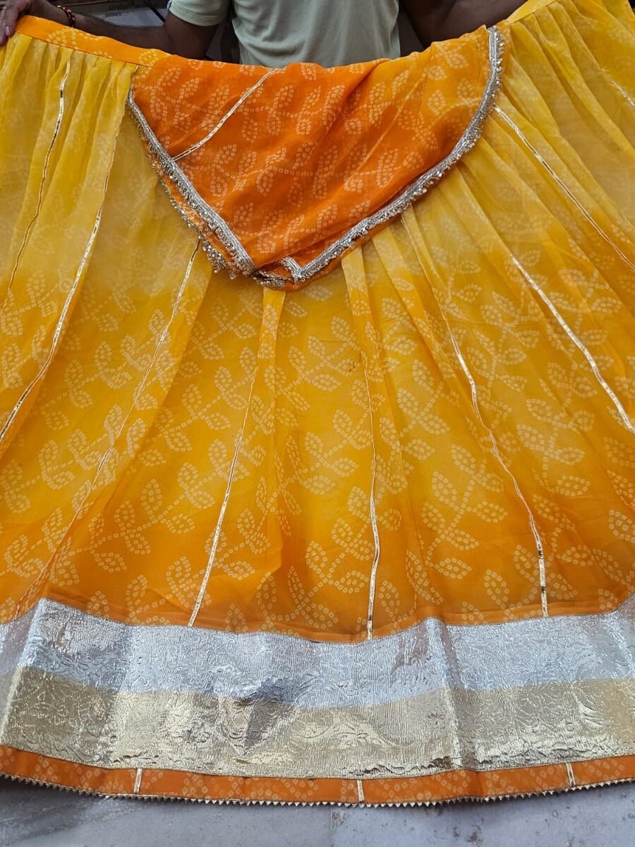 A yellow and orange Bandhani lehenga featuring a wide silver and gold Lappa lace border on display.