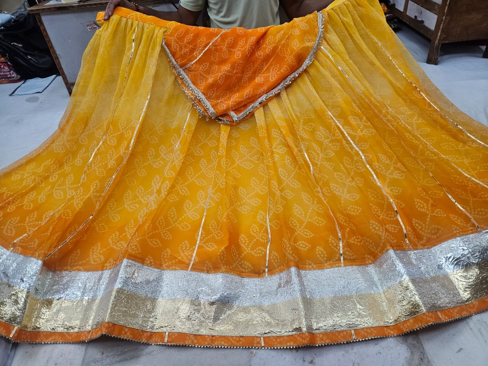 Royal Jorjet Bandhani Lehenga with Lappa Lace Border 1 A yellow and orange Bandhani lehenga featuring a wide silver and gold Lappa lace border on display.