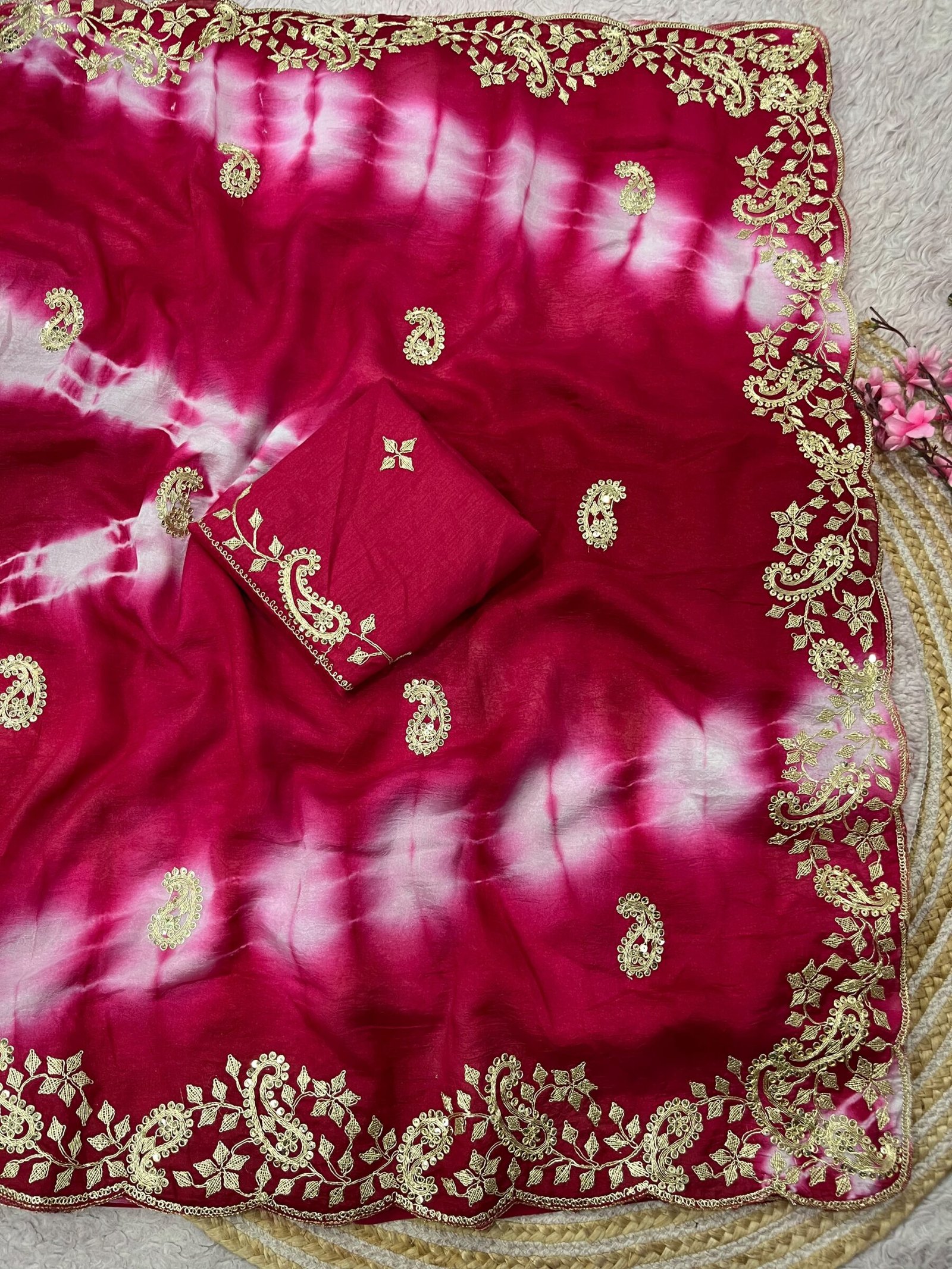 Tana Bana Fabric Saree with Pitta and Sequence Work 6 Four vibrant tie-dye sarees in yellow, orange, purple, and maroon, each featuring heavy gold embroidery and cutwork borders, displayed on a circular woven mat.