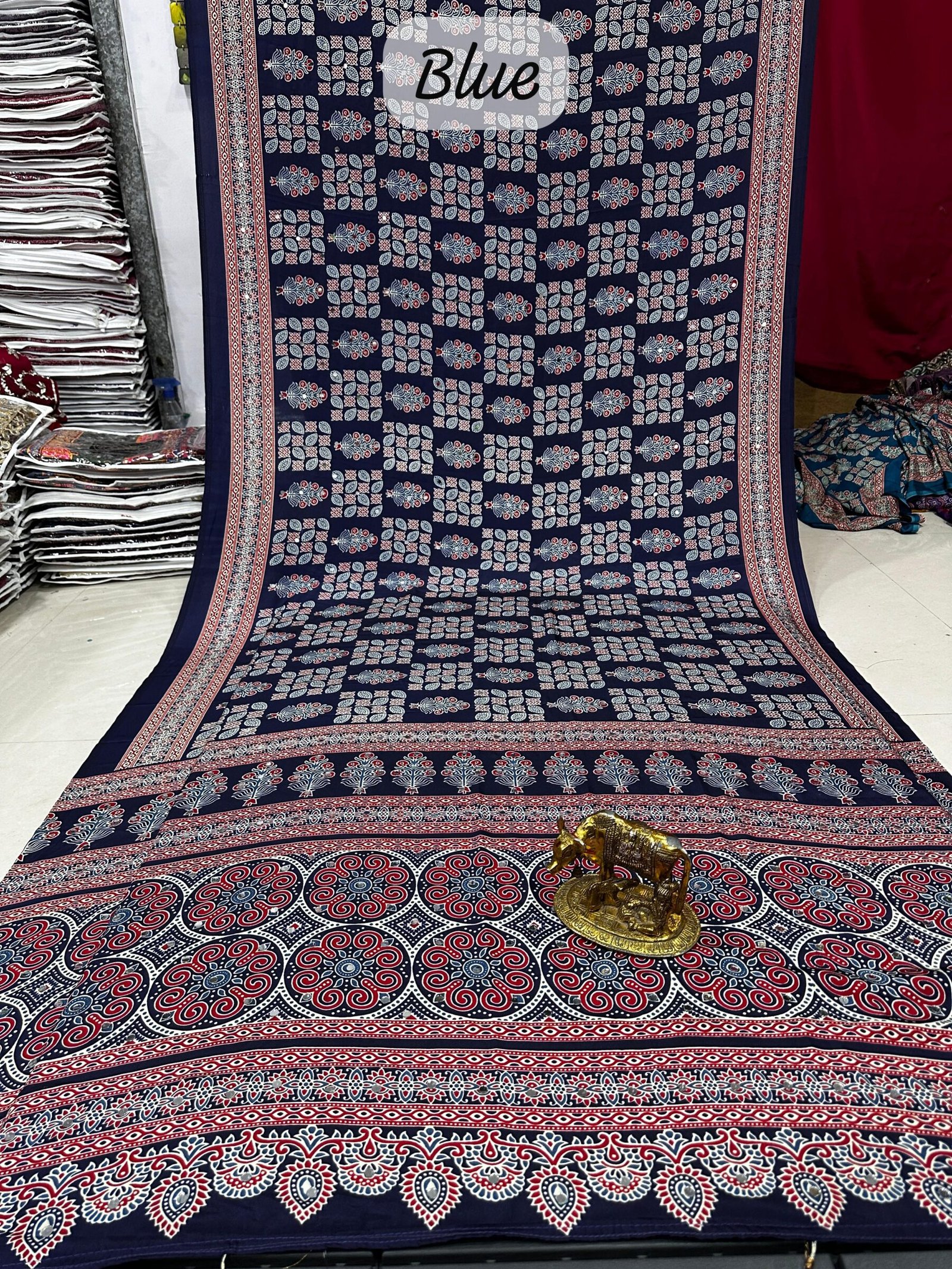 Ajarkh Print Soft Satin Silk Saree with Mirror Work 2 A maroon Ajarkh print soft satin silk saree displayed with a golden statue of a bull, featuring intricate mirror work and traditional patterns.