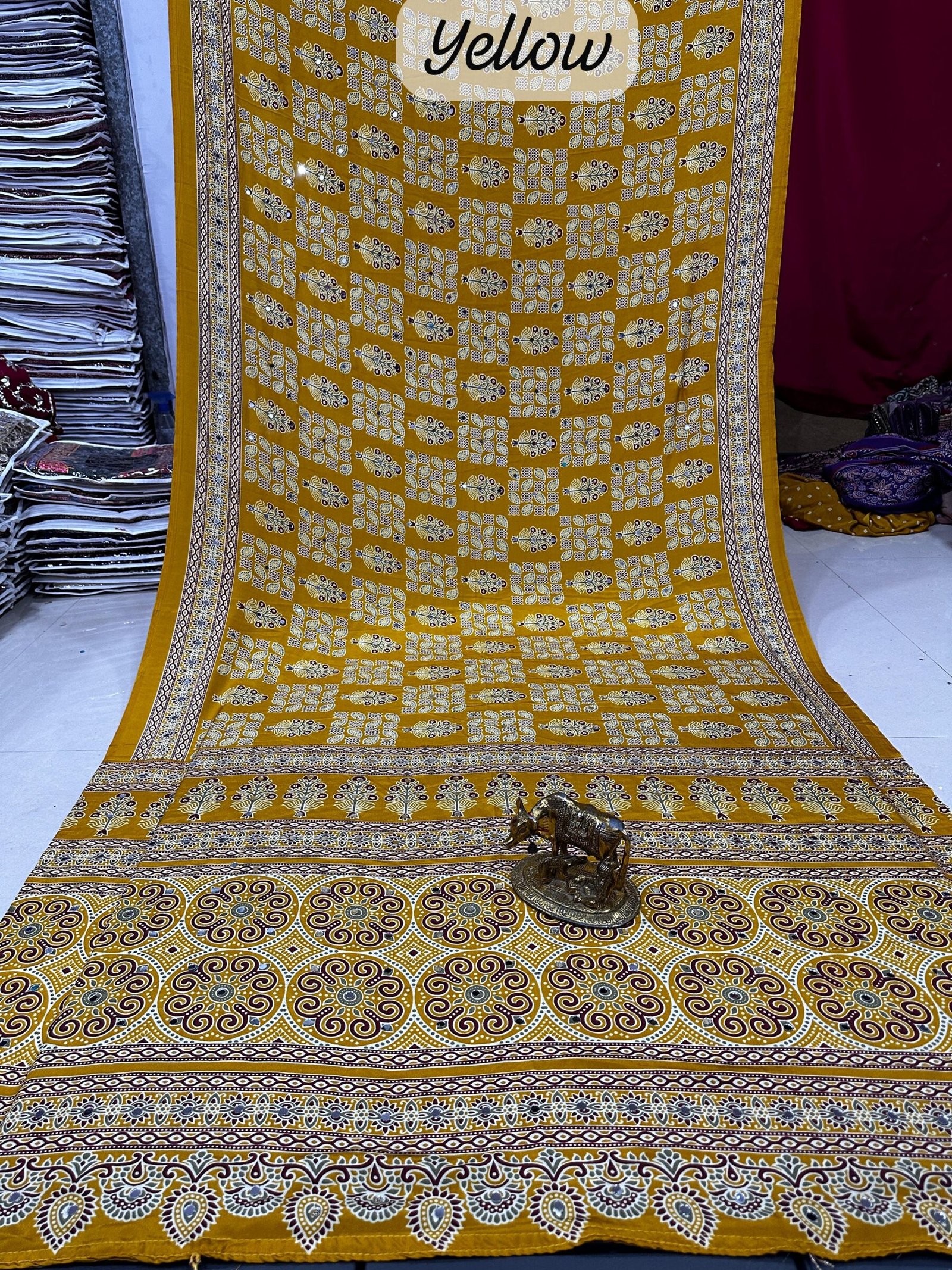 Ajarkh Print Soft Satin Silk Saree with Mirror Work 3 A maroon Ajarkh print soft satin silk saree displayed with a golden statue of a bull, featuring intricate mirror work and traditional patterns.