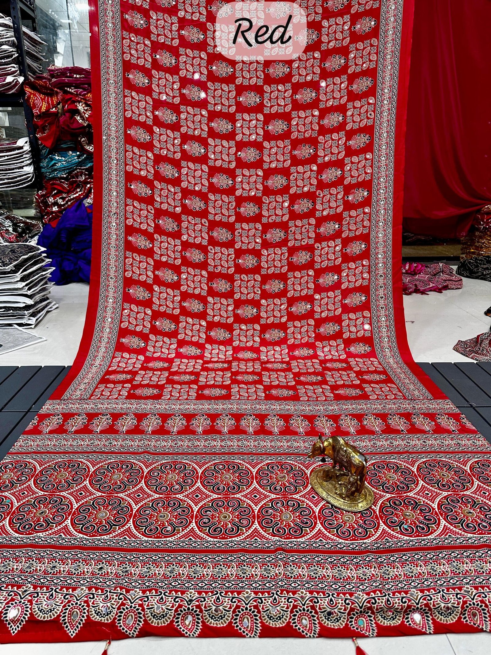 Ajarkh Print Soft Satin Silk Saree with Mirror Work 4 A maroon Ajarkh print soft satin silk saree displayed with a golden statue of a bull, featuring intricate mirror work and traditional patterns.