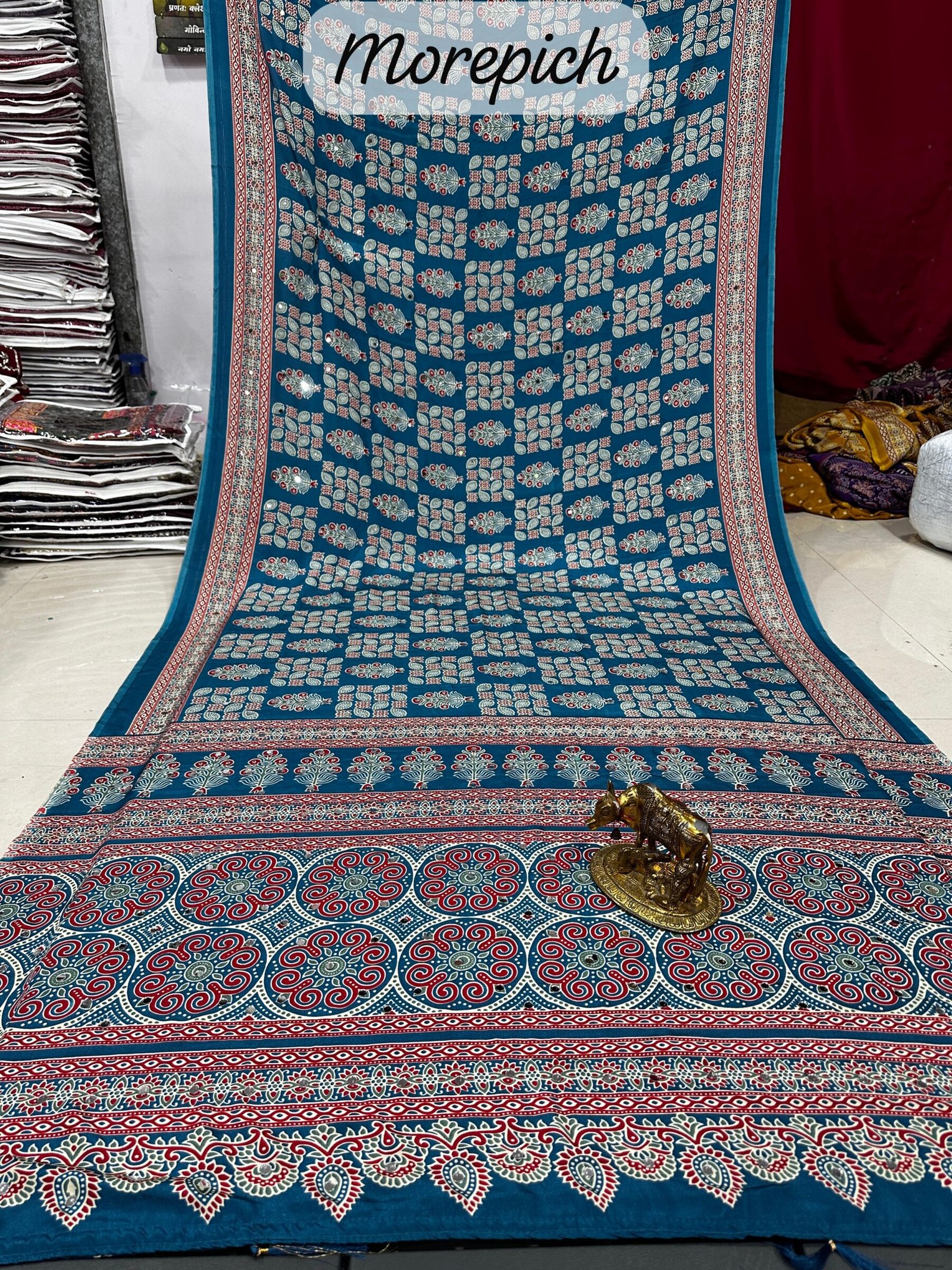 Ajarkh Print Soft Satin Silk Saree with Mirror Work 7 A maroon Ajarkh print soft satin silk saree displayed with a golden statue of a bull, featuring intricate mirror work and traditional patterns.