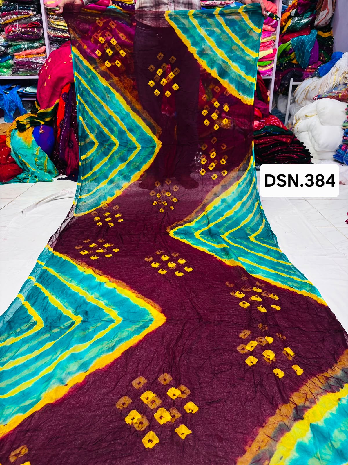 Art Silk Bandhani Saree 1 A person holding up a vibrant art silk Bandhani saree with geometric patterns and bright tie-dye work.
