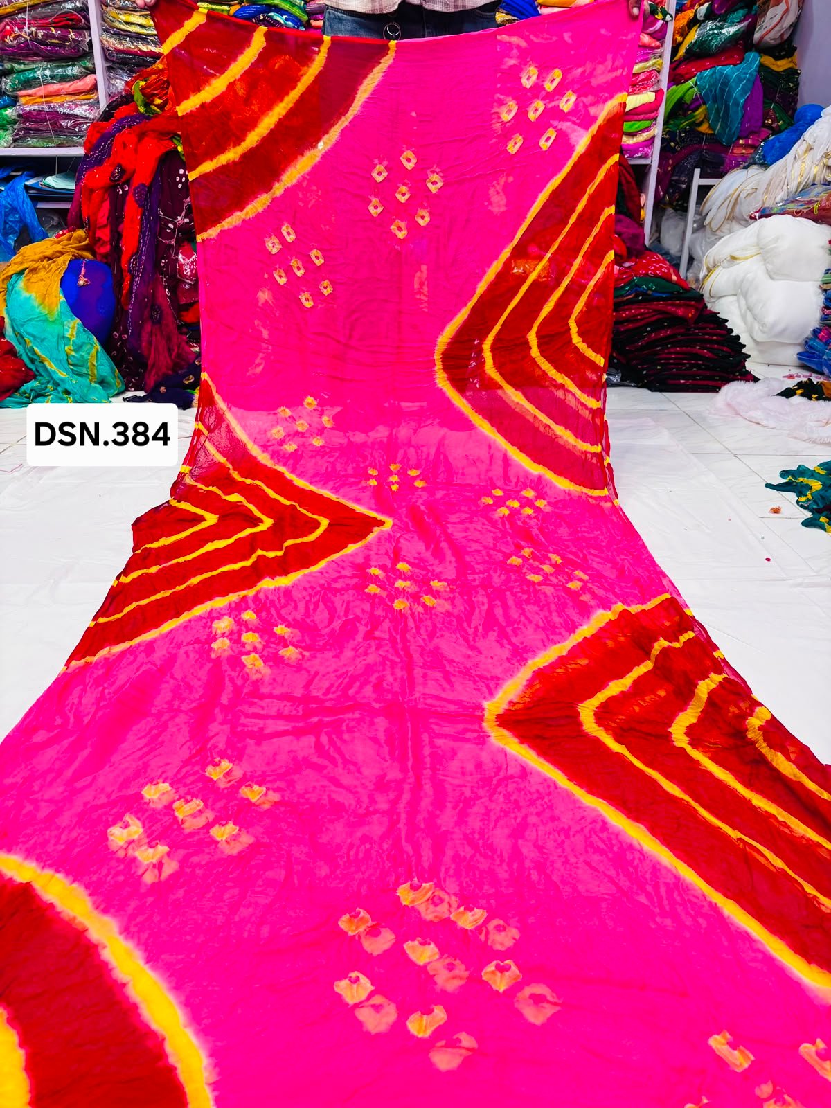 Art Silk Bandhani Saree 2 A person holding up a vibrant art silk Bandhani saree with geometric patterns and bright tie-dye work.