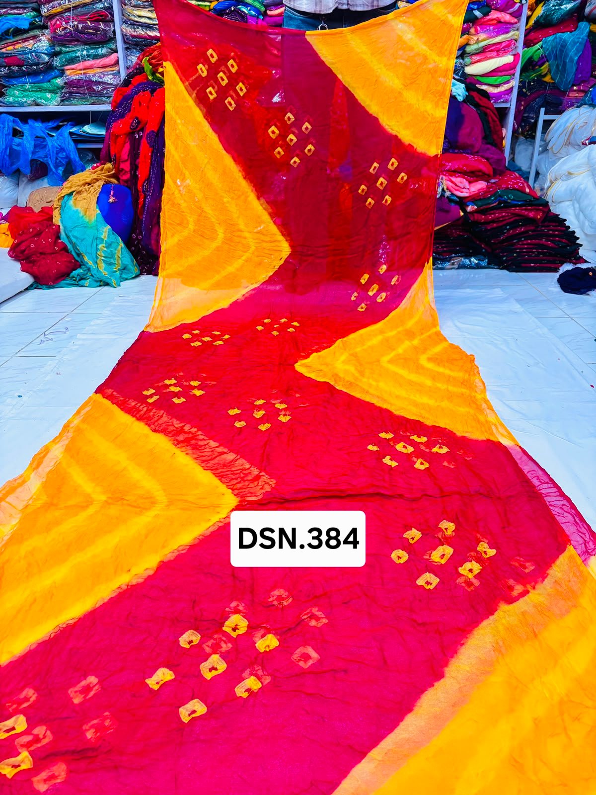 Art Silk Bandhani Saree 3 A person holding up a vibrant art silk Bandhani saree with geometric patterns and bright tie-dye work.
