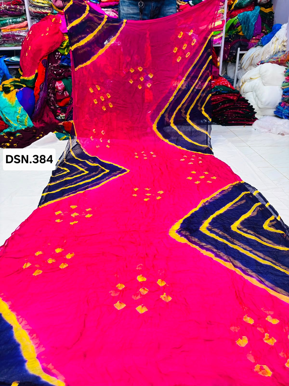 Art Silk Bandhani Saree 4 A person holding up a vibrant art silk Bandhani saree with geometric patterns and bright tie-dye work.