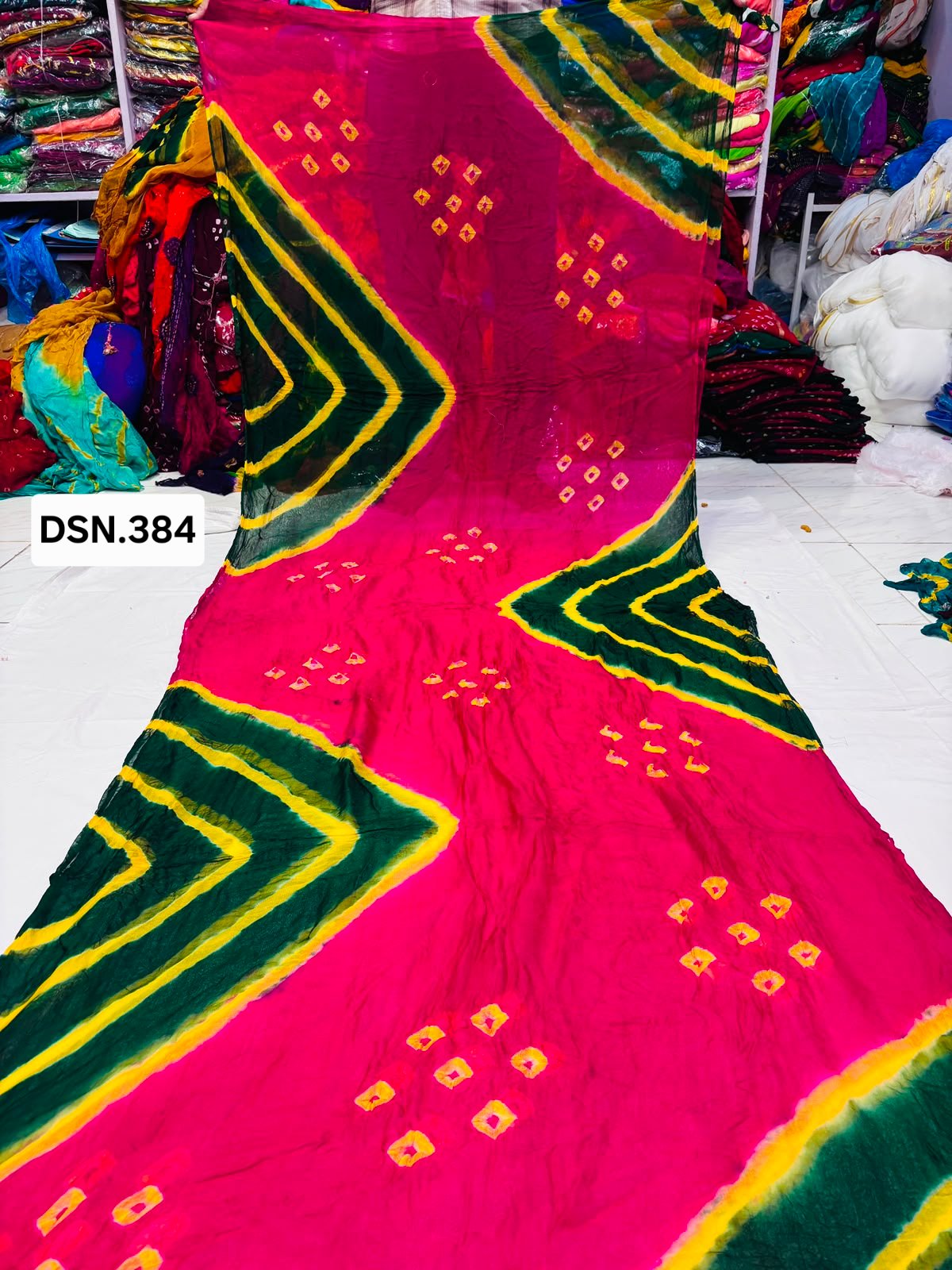 Art Silk Bandhani Saree 7 A person holding up a vibrant art silk Bandhani saree with geometric patterns and bright tie-dye work.