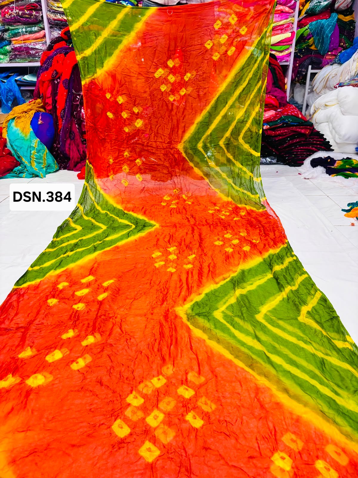 Art Silk Bandhani Saree 8 A person holding up a vibrant art silk Bandhani saree with geometric patterns and bright tie-dye work.