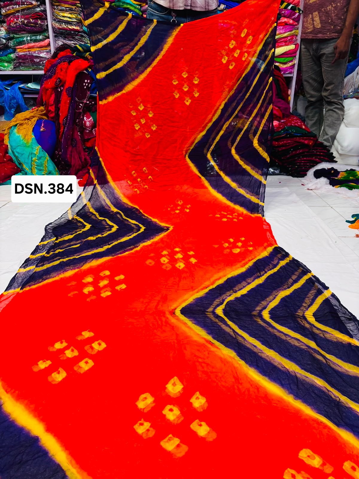 Art Silk Bandhani Saree 9 A person holding up a vibrant art silk Bandhani saree with geometric patterns and bright tie-dye work.