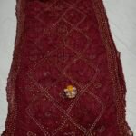 A beautiful deep maroon Art Silk Rai Bandhej Saree displayed with a small idol placed on top to highlight its intricate patterned texture.