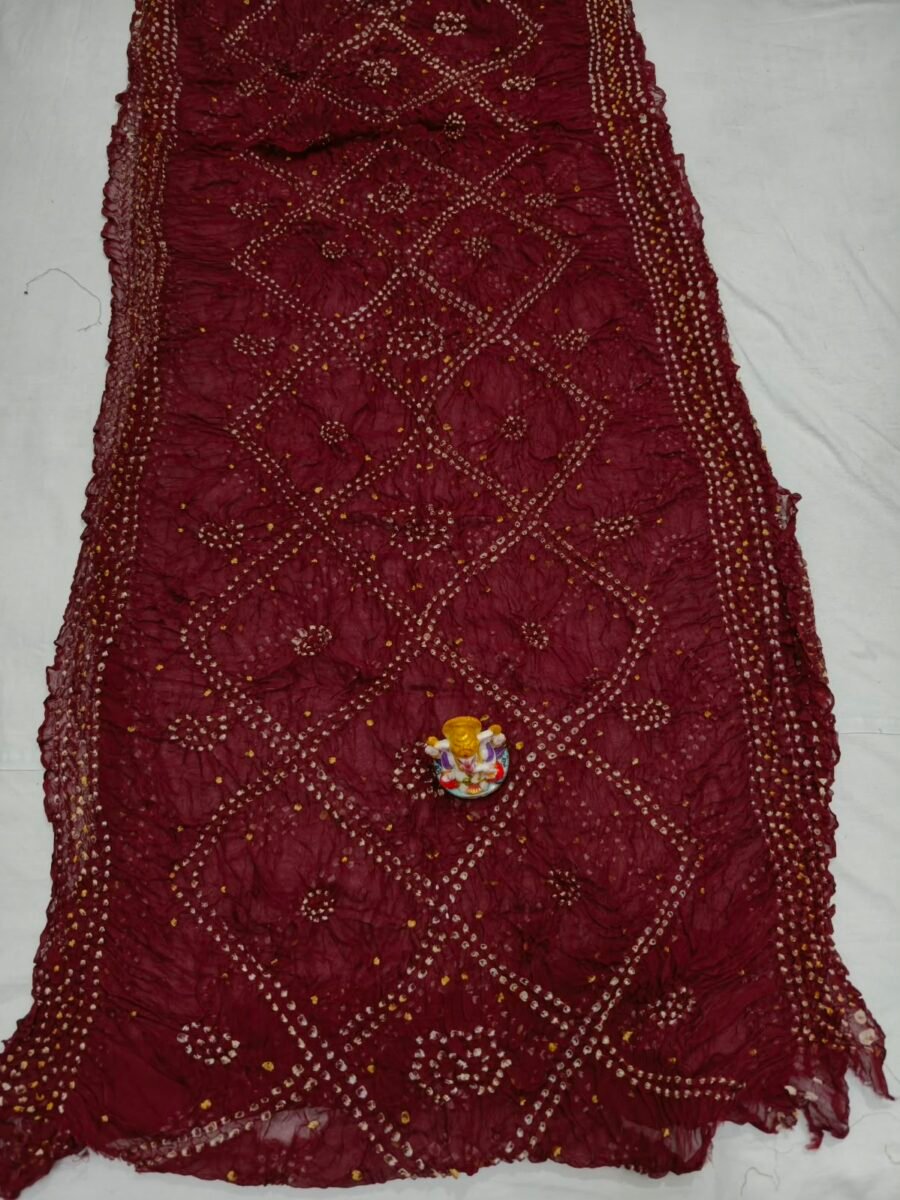 New Arrivals 47 A beautiful deep maroon Art Silk Rai Bandhej Saree displayed with a small idol placed on top to highlight its intricate patterned texture.