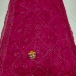 A beautiful deep maroon Art Silk Rai Bandhej Saree displayed with a small idol placed on top to highlight its intricate patterned texture.