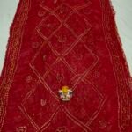 A beautiful deep maroon Art Silk Rai Bandhej Saree displayed with a small idol placed on top to highlight its intricate patterned texture.