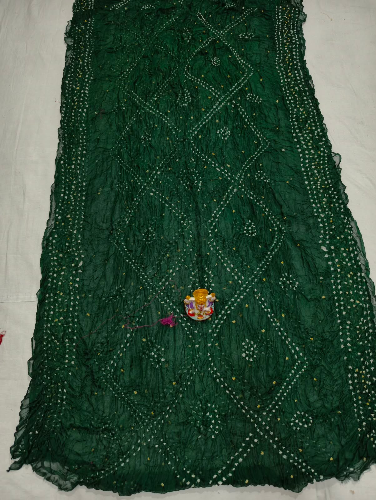 Art Silk Rai Bandhej Saree | Traditional Bandhani Drape 6 A beautiful deep maroon Art Silk Rai Bandhej Saree displayed with a small idol placed on top to highlight its intricate patterned texture.