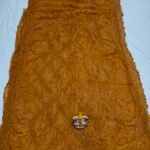 A beautiful deep maroon Art Silk Rai Bandhej Saree displayed with a small idol placed on top to highlight its intricate patterned texture.