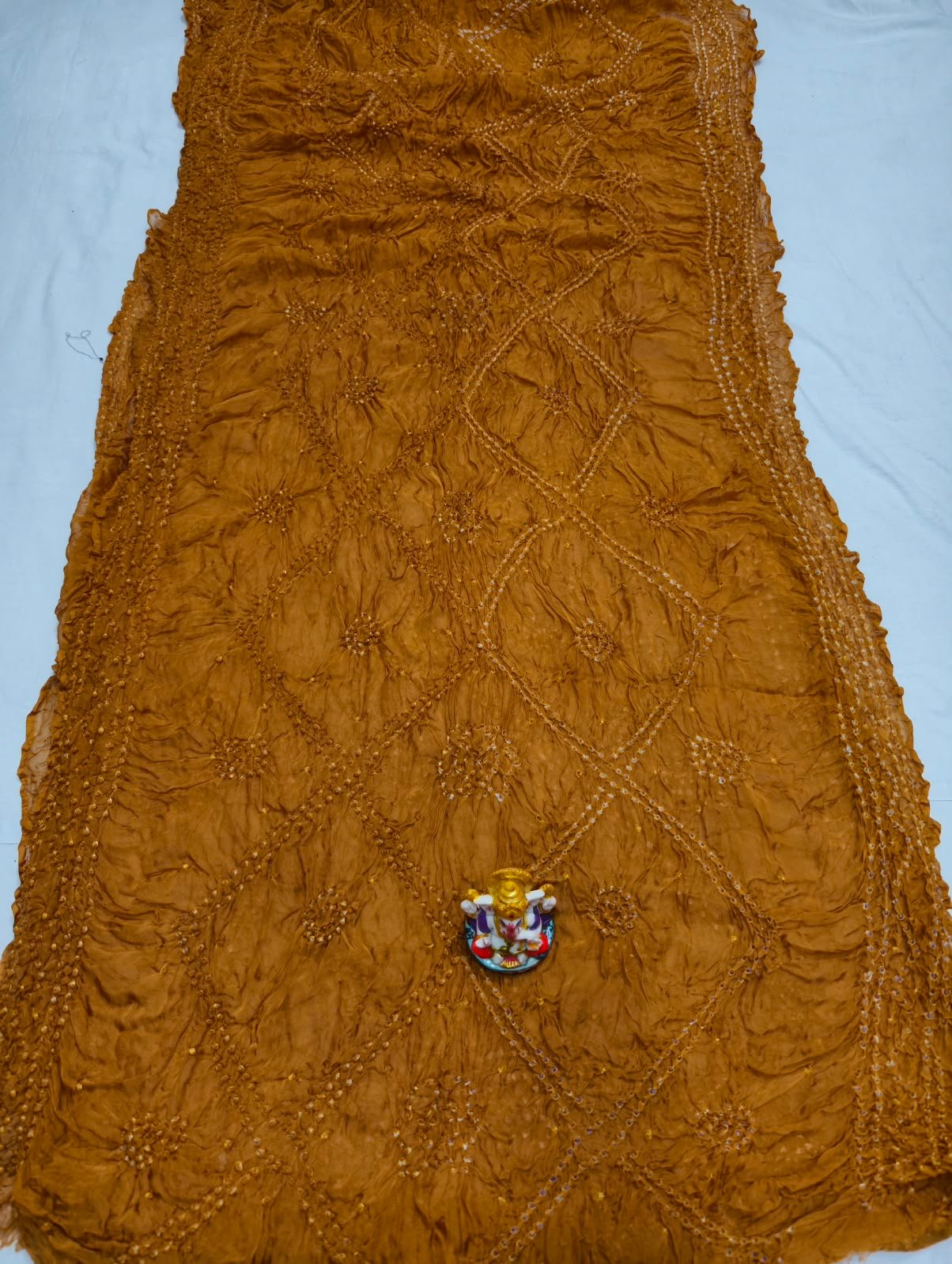 Art Silk Rai Bandhej Saree | Traditional Bandhani Drape 7 A beautiful deep maroon Art Silk Rai Bandhej Saree displayed with a small idol placed on top to highlight its intricate patterned texture.