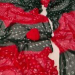 A close-up of a Nazneen Chiffon Bandhani Saree featuring vibrant red and yellow tie and dye patterns.