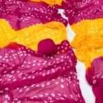 A close-up of a Nazneen Chiffon Bandhani Saree featuring vibrant red and yellow tie and dye patterns.