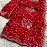 A close-up view of a vibrant red synthetic georgette saree featuring intricate Bandhani prints, silver handwork motifs, and an elaborate cutwork border.
