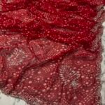 A close-up view of a vibrant red synthetic georgette saree featuring intricate Bandhani prints, silver handwork motifs, and an elaborate cutwork border.