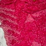 A close-up view of a vibrant red synthetic georgette saree featuring intricate Bandhani prints, silver handwork motifs, and an elaborate cutwork border.