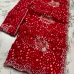 A close-up view of a vibrant red synthetic georgette saree featuring intricate Bandhani prints, silver handwork motifs, and an elaborate cutwork border.