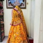 A red and yellow Bandhani lehenga with Gota Patti work displayed on a mannequin.