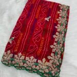 A beautiful red Bandhej saree with heavy coding, sequence work, and a wide embroidered floral border displayed on a white fur background.