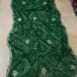 Four vibrant Bandhej sarees in red, pink, blue, and green with heavy Gota Patti borders lying on a floor.